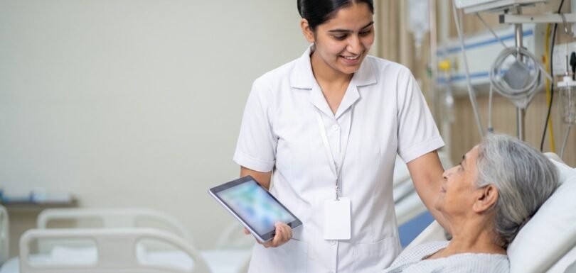 Nurse using a tablet at a patient's bedside while speaking kindly with the patient in an Indian hospital ward